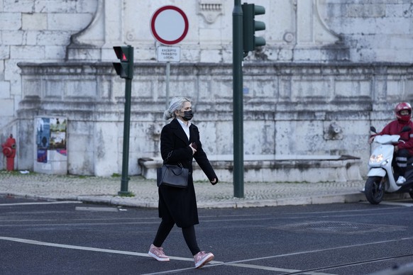 A woman wearing a face mask crosses a street in Lisbon, Thursday, Nov. 25, 2021. Portugal is reporting its highest number of new daily COVID-19 infections since July amid a surge in cases across Europe. The Portuguese government is due to announce on Thursday what new pandemic restrictions it is introducing, seven weeks after scrapping almost all of them due to the high vaccination rate. (AP Photo/Armando Franca)