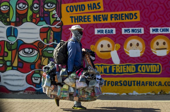 A street vendor carrying merchandise walks past a mural on how to wear a face mask to prevent the spread of coronavirus, in Soweto, South Africa, Saturday, May 15, 2021. (AP Photo/Themba Hadebe)