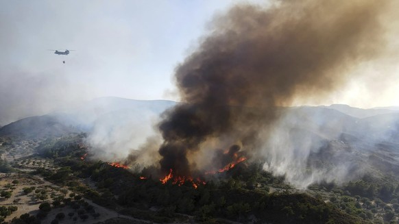 A military helicopter operates as flames burn a forest on the mountains near Vati village, on the Aegean Sea island of Rhodes, southeastern Greece, on Tuesday, July 25, 2023. (AP Photo/Spiros Tsampika ...