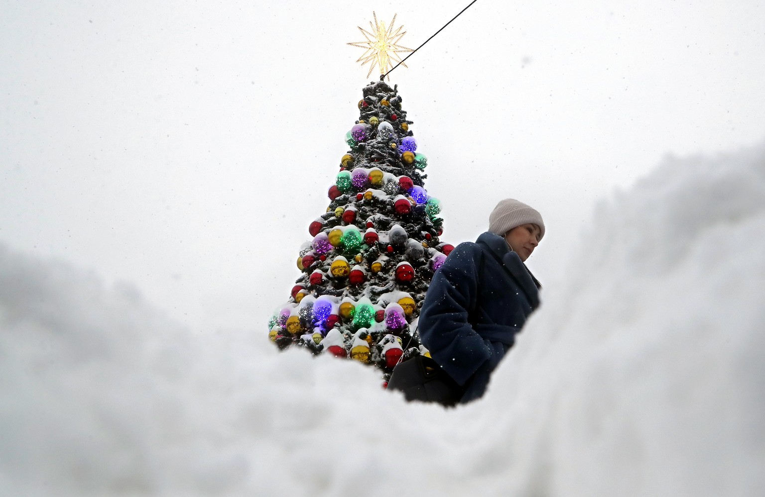 epa11030859 A woman walks in front of a snow-covered Christmas tree during a heavy snow fall in Moscow, Russia, 15 December 2023. According to meteorologists, one of the biggest snow falls in decades  ...