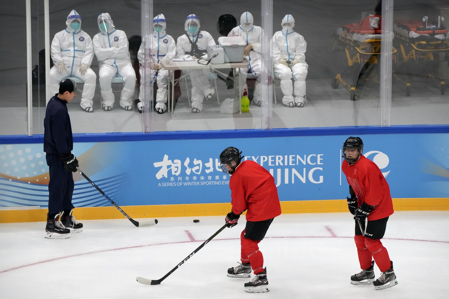 Medical personnel in protective suits watch as the China Ice Sports College hockey team practices on the ice during the Experience Beijing Ice Hockey Domestic Test Activity, a test event for the 2022  ...