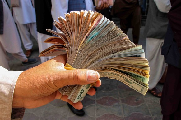 epa09463588 A currency exchange dealer counts Afganis as people gather to withdraw money from a bank in Kabul, Afghanistan, 12 September 2021. The country has been experiencing a severe humanitarian c ...