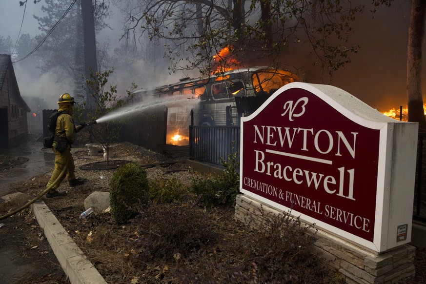 epa07152484 A fire fighter puts water on a fire as he as he performs structure protection, as the Camp Fire burns out of control through Paradise, fueled by high winds in Butte County, California, USA ...