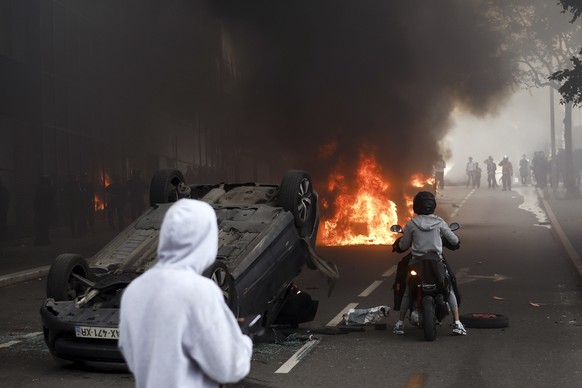 epaselect epa10717564 A fire burns next to an overturned car during clashes with French riot police following a march in the memory of 17-year-old Nahel, who was killed by French Police in Nanterre, n ...
