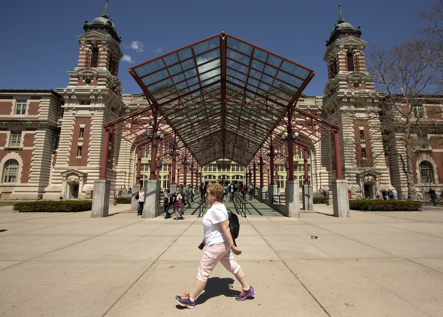 Tourists walk around the grounds at Ellis Island, Wednesday, April 29, 2015, in New York. With the unveiling of a new exhibition next month, Ellis Island is telling stories of immigrants who have come ...