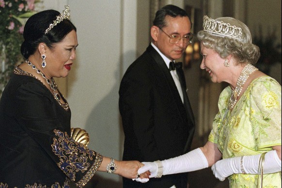 FILE - British Queen Elizabeth II, right, smiles as she greets Thai Queen Sirikit, left, with Thai King Bhumibol Adulyadej looking on at a reception at the British Ambassador&#039;s residence in centr ...