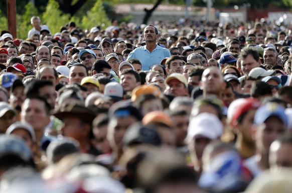 A man peaks over the crowd waiting to cross the border into Colombia through the Simon Bolivar bridge in San Antonio del Tachira, Venezuela Sunday July 17, 2016. Tens of thousands of Venezuelans cross ...