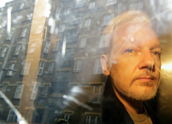 FILE - Buildings are reflected in the window as WikiLeaks founder Julian Assange is led away from the court where he appeared seven years ago on charges of breaking British bail, in London, on May 1, 2019. A...