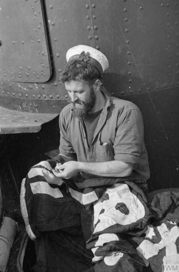 Adding Another Success Bar To Submarine Taku&#039;s Jolly Roger. February and March 1943, at HMS Talbot, Malta. One of the crew of the British submarine TAKU sewing another success bar to their Jolly  ...