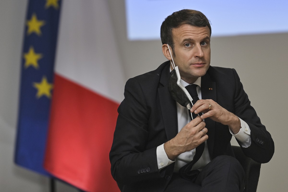 French President Emmanuel Macron removes a protective face mask to take a drink of water as he attends a meeting during a visit at the headquarters of the local CAF (French family allowance public ser ...