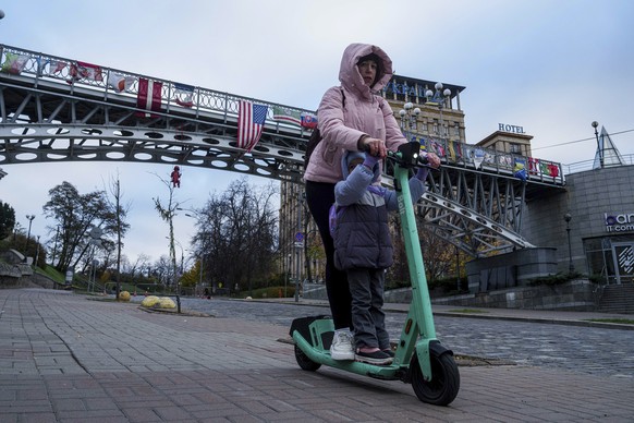 A woman with her child rides on an electric scooter in Kyiv, Ukraine, Wednesday, Nov. 6, 2024. (AP Photo/Evgeniy Maloletka)