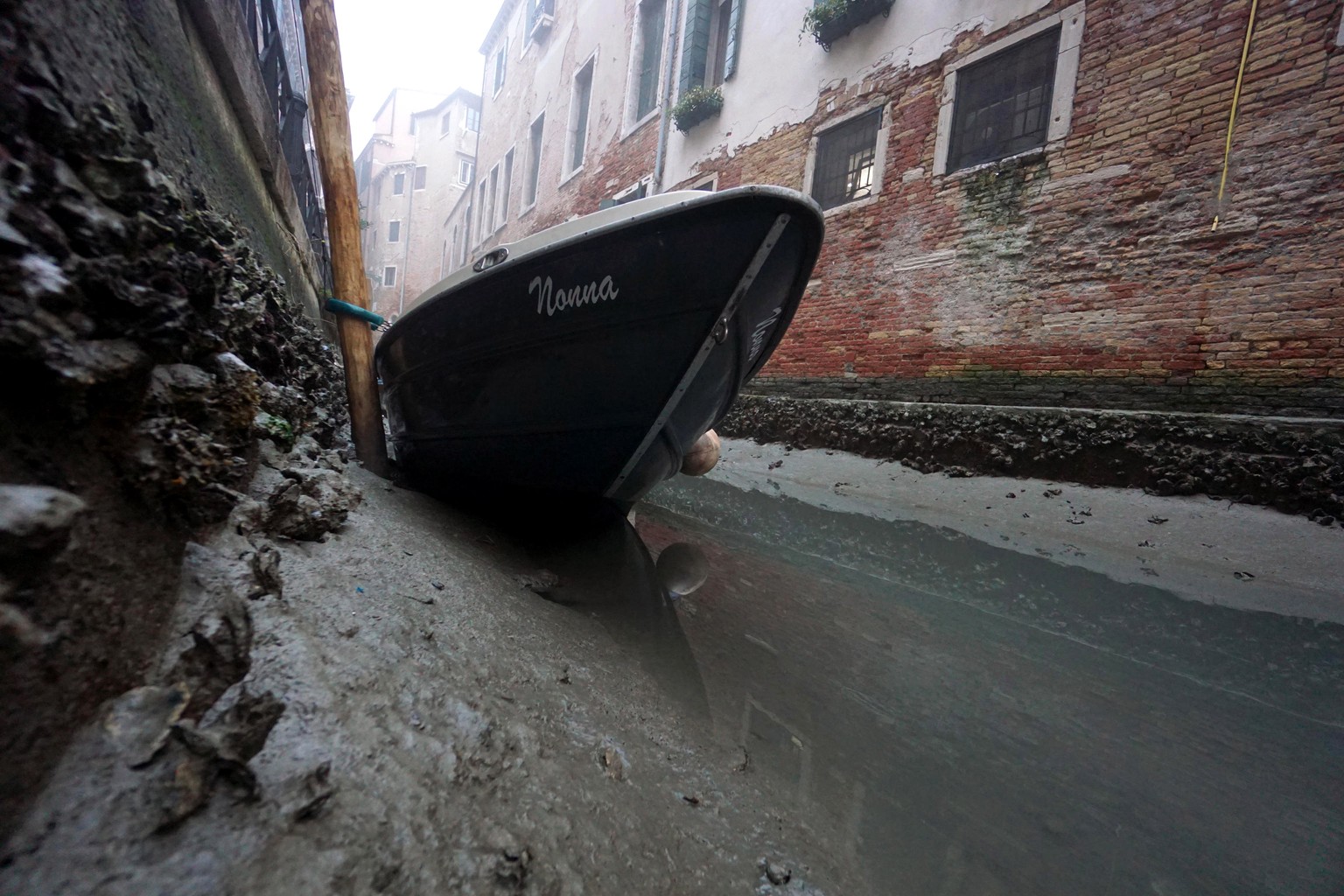 epa10473371 A small boat lies on the bottom of an internal canal during a low tide in Venice, Italy, 17 February 2023. Venice has been struggling for many days with a low tide, which is beginning to c ...
