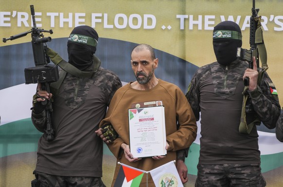 Israeli captive, Eli Sharabi, who has been held hostage by Hamas in Gaza since October 7, 2023, stands on a stage escorted by Hamas fighters before being handed over to the Red Cross in Deir al-Balah, ...