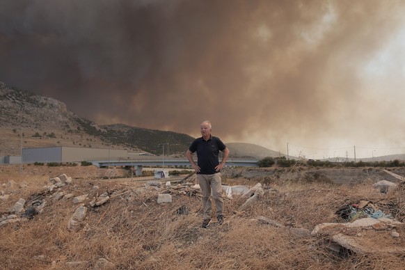 epa10813329 A local resident looks at a wildfire in the industrial zone of Aspropyrgos near Athens, Greece, 22 August 2023. A wildfire is in progress in Fyli, west Attica region. So far, 26 firefighte ...