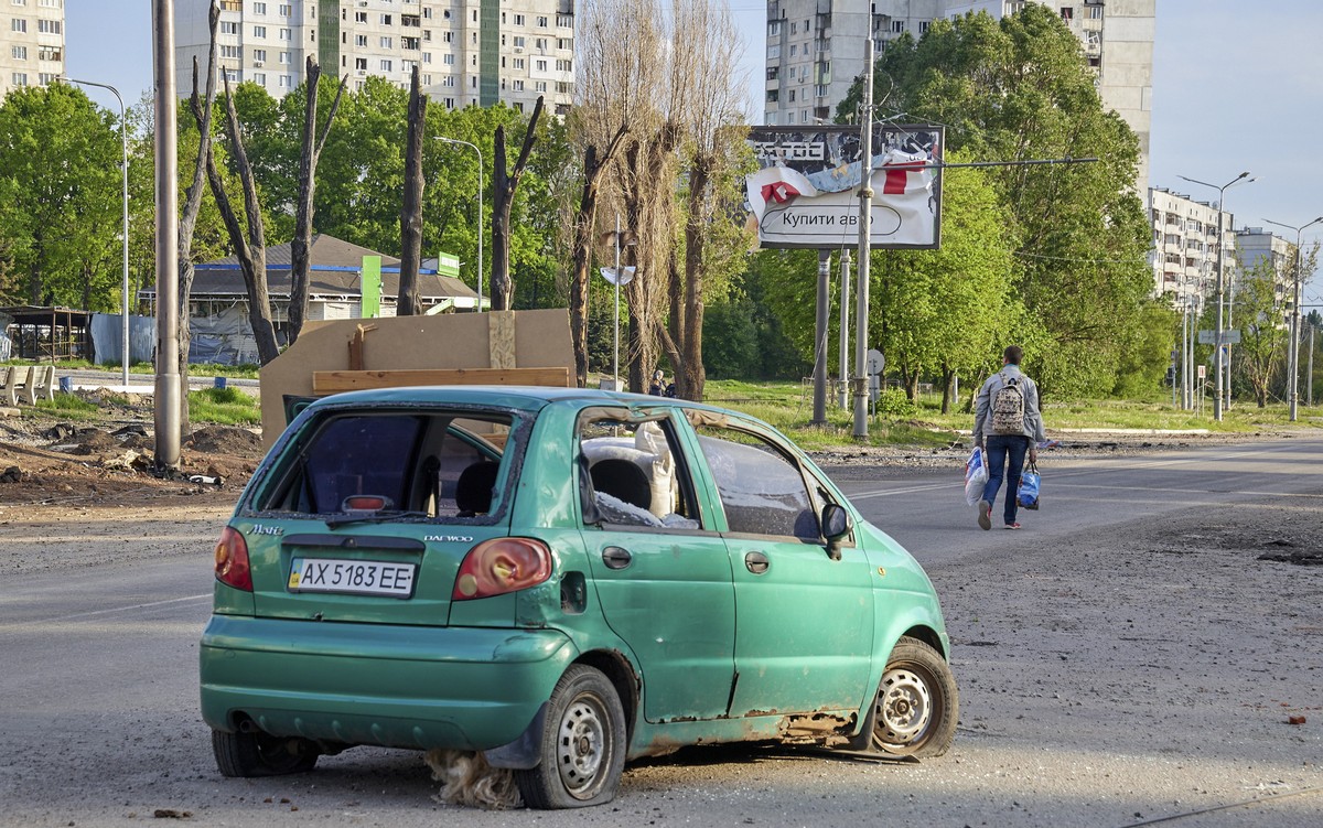 epa09947554 A man carries things as he walks on a street, past a damaged car, on the outskirts of Kharkiv, Ukraine, 14 May 2022. Kharkiv, Ukraine's second-largest city, has witnessed repeated air ...
