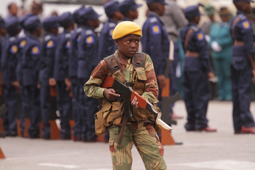 A young boy dressed as a soldier stands guard while holding a wooden gun during the opening of the 23rd session of the Junior Parliament of Zimbabwe in Harare, Saturday, June, 20, 2015. The Junior par ...