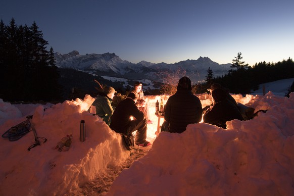 A group of person look at a campfire with the view of Alps, during the sunset near Ensex, above Villars-sur-Ollon, Switzerland, Saturday, 18 February 2017. (KEYSTONE/Anthony Anex)