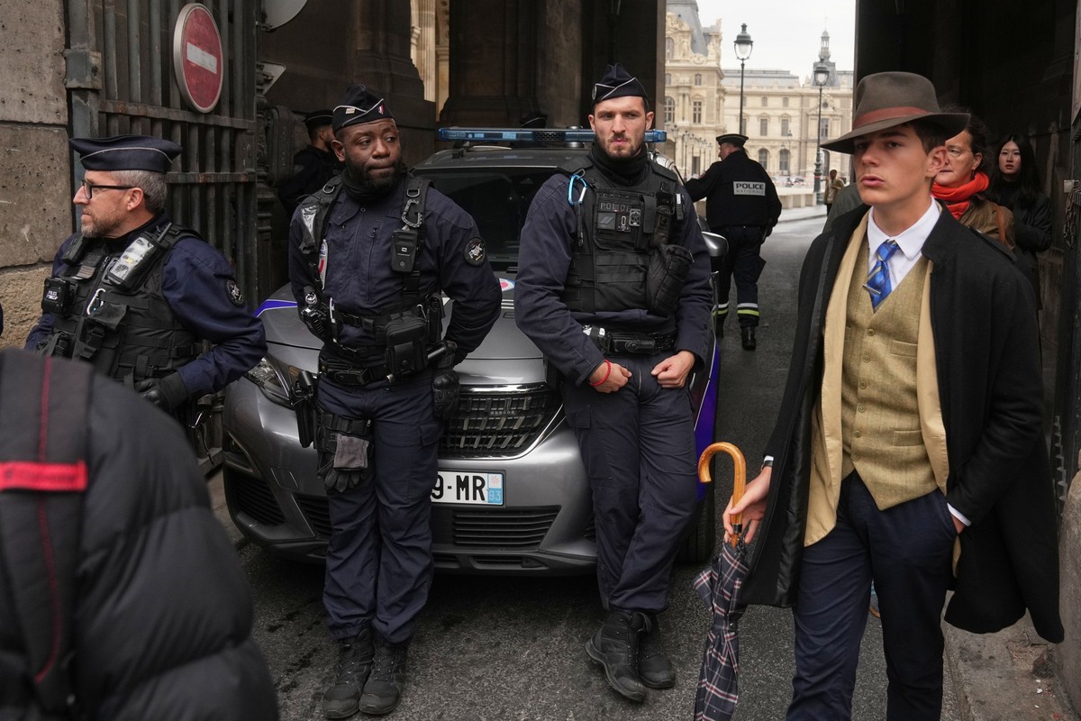 L'homme, vêtu d'un gilet boutonné, d'un trench-coat et d'un fedora, qui semblait surveiller la scène, a déclenché l'indignation sur Internet. (AP Photo/Thibault Camus)