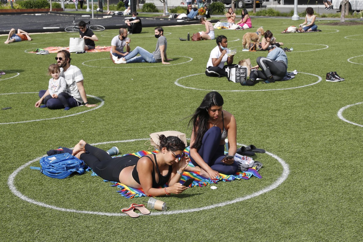 Two young women relax in a circle marked on the grass for proper social distancing in Brooklyn's Domino Park as others do the same to prevent the spread of coronavirus, Monday, May 18, 2020, in N ...