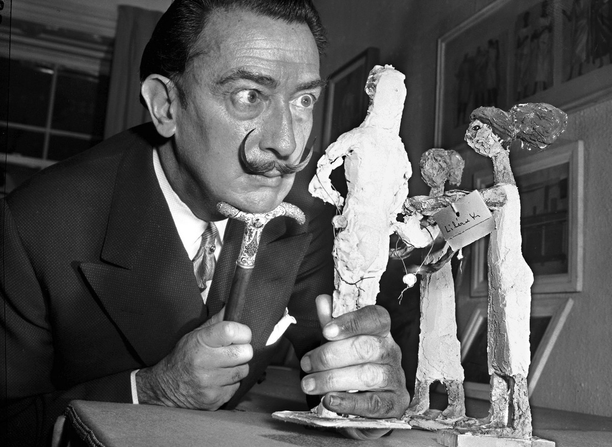 Resting his chin on the handle of his cane, Spanish surrealist painter Salvador Dali studies an exhibit of contemporary Greek art in New York, Jan. 4, 1956. Dali called his trademark mustache his &quo ...