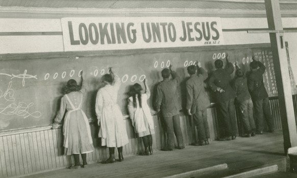 In this 1910s photo provided by the United Church of Canada Archives, students write on a chalkboard at the Red Deer Indian Industrial School in Alberta. In Canada, where more than 150,000 Indigenous  ...