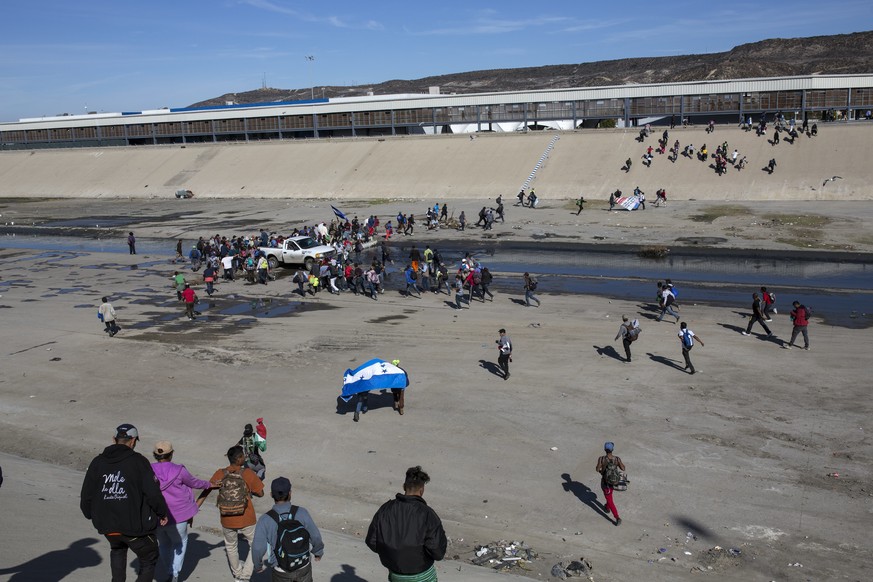 Migrants walk across a riverbank at the Mexico-U.S. border after getting past a line of Mexican police at the Chaparral border crossing in Tijuana, Mexico, Sunday, Nov. 25, 2018, as they try to reach  ...