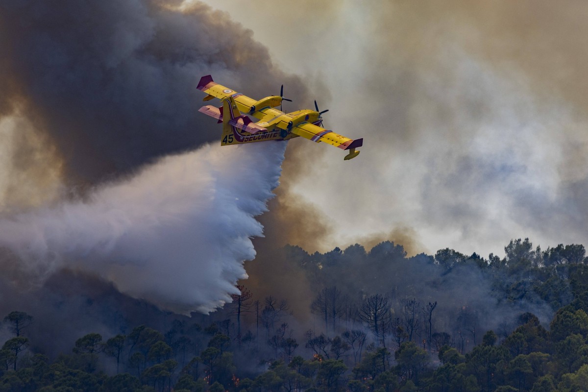Wildfires in the Var - France Aerial firefighting plane marked Securite Civile drops water over a burning forest during a wildfire in Cotignac, thick smoke, flames and trees are visible below the airc ...