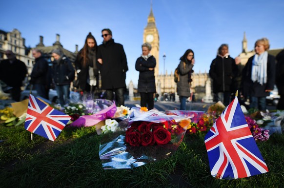 epa05868191 People stand by to look at flowers and Union jack flags placed on Parliament square by well-wishers in London, Britain, 24 March 2017. Well-wishers have flocked to the scene of the 22 Marc ...