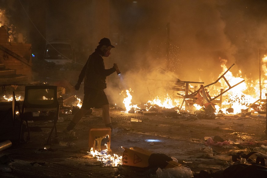 A protester walks past burning debris as police storm part of the Hong Kong Polytechnic University campus during the early morning hours in Hong Kong, Monday, Nov. 18, 2019. Police breached the univer ...