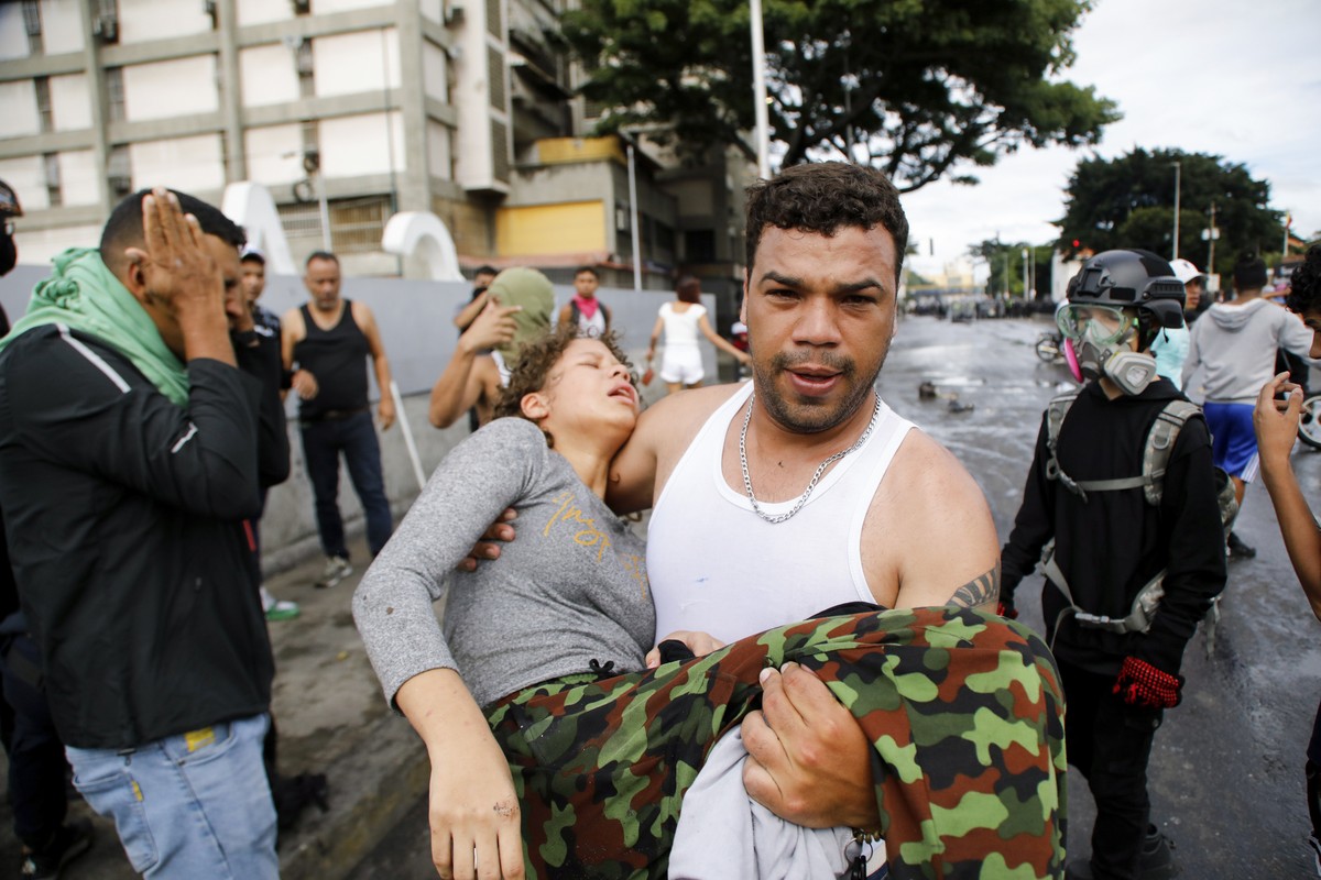 A man carries a protester affected by tear gas thrown by police during demonstrations against the official election results declaring President Nicolas Maduro's reelection, the day after the vote ...