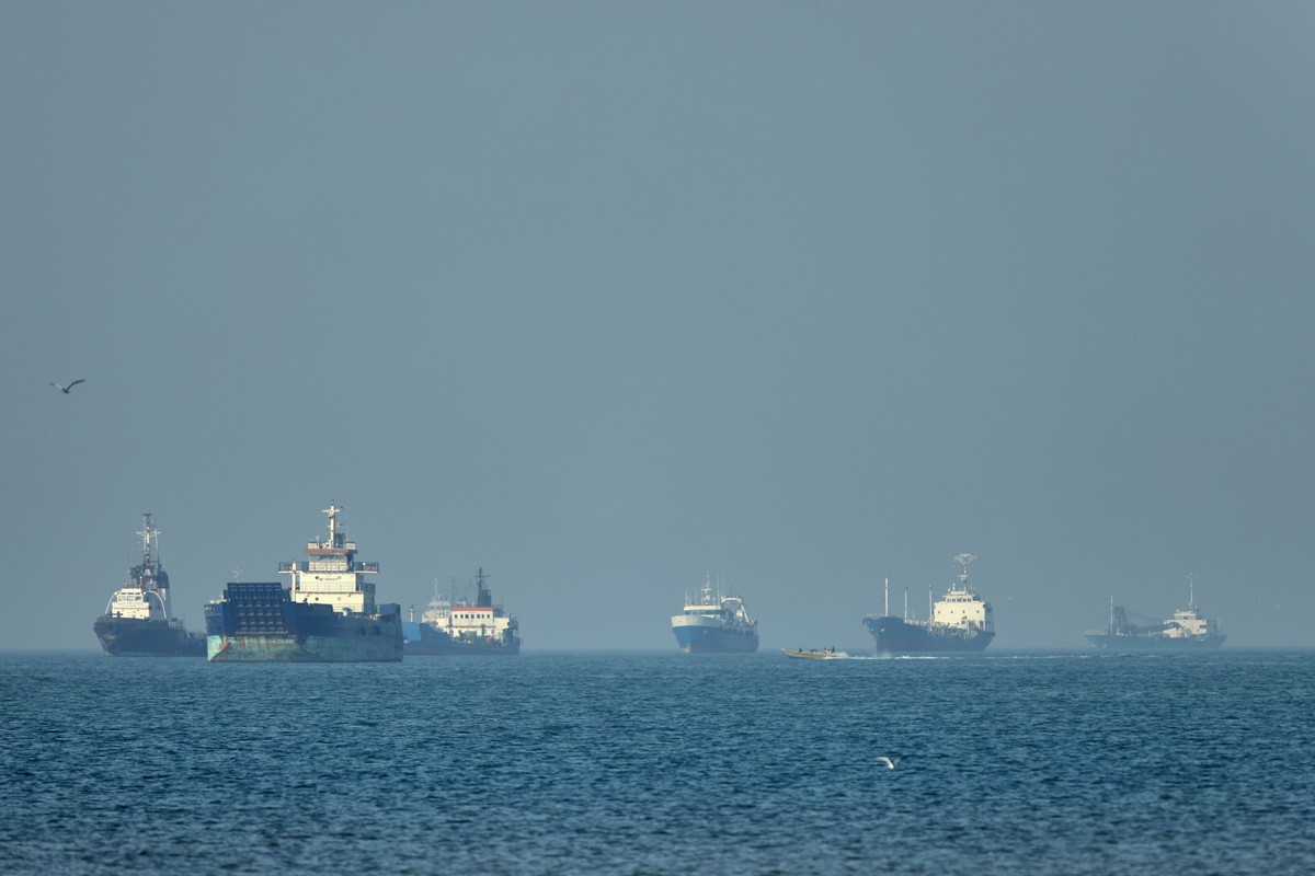 KEYPIX - Cargo ships, including bulk carriers and general cargo vessels, sit at anchor offshore as a small motorboat passes in the foreground, in the Strait of Hormuz off Bandar Abbas, Iran, Monday, M ...