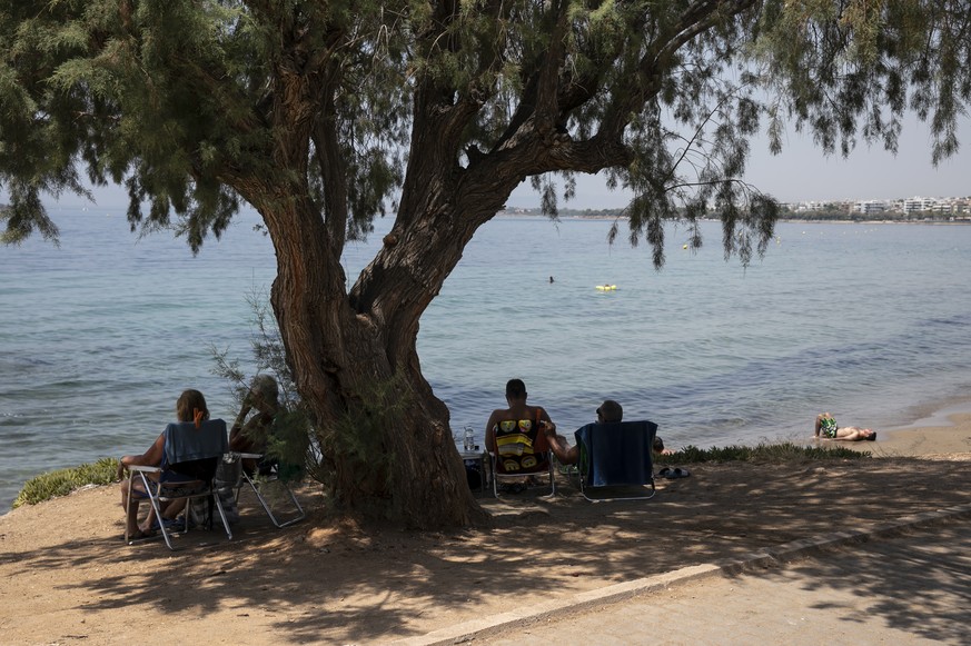 A man sunbathes as others sit under a pine tree at a beach of Kavouri suburb, southwest of Athens, on Friday, July 30, 2021. Greek authorities ordered additional fire patrols and infrastructure mainte ...