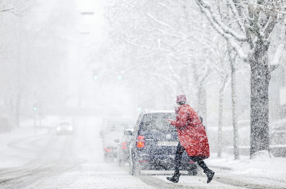 A woman is crossing a road during snowfall in Zuerich on Friday, December 10, 2021. (KEYSTONE/Michael Buholzer)