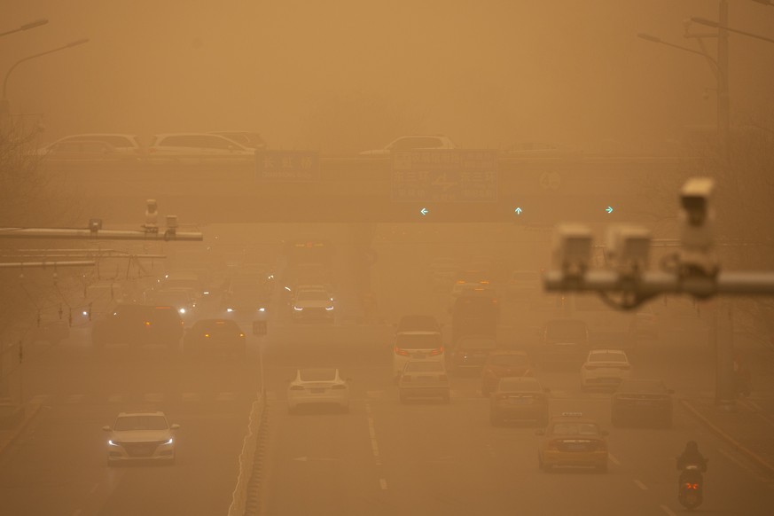 Cars are driven along a street amid a sandstorm during the morning rush hour in Beijing, Monday, March 15, 2021. The sandstorm brought a tinted haze to Beijing's skies and sent air quality indice ...