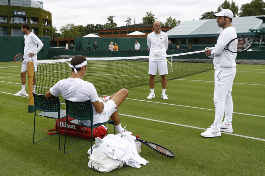 Roger Federer of Switzerland sits on his chair next to his coaches Severin Luethi, right, and Ivan Ljubicic, center, during a training session, at the All England Lawn Tennis Championships in Wimbledo ...