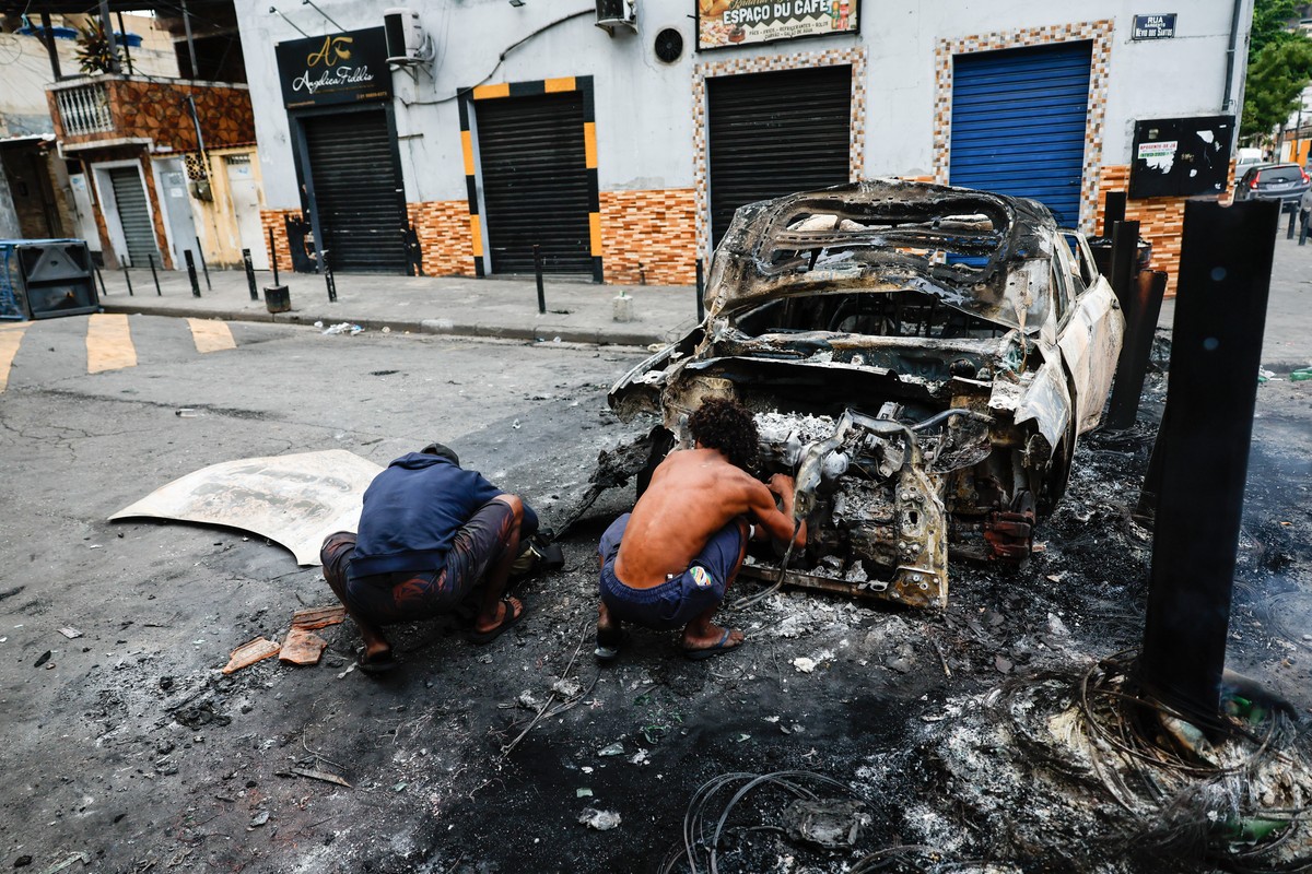 epa12488604 People take cover behind a burned-out vehicle during a police operation in Rio de Janeiro, Brazil, 28 October 2025. At least 64 people have been killed and 81 arrested in what officials de ...