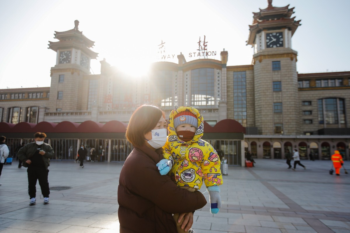 epa10397596 A woman wearing a face mask holds a child in front of the Beijing Railway Station in Beijing, China, 10 January 2023. Chinese passengers are travelling domestically as the nation's mo ...