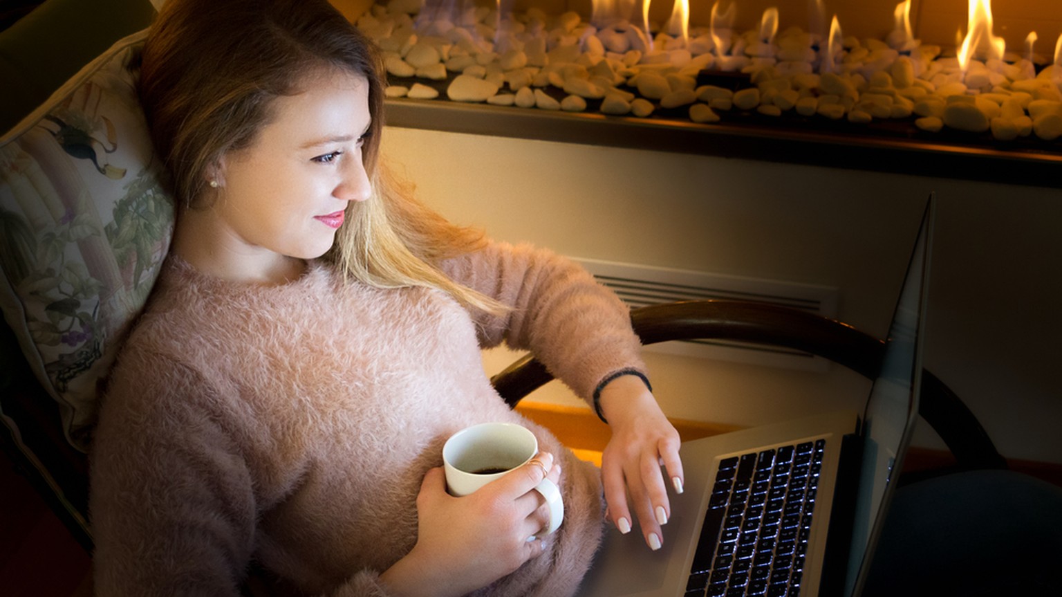 Frau mit Laptop vor Cheminée (Symbolbild)