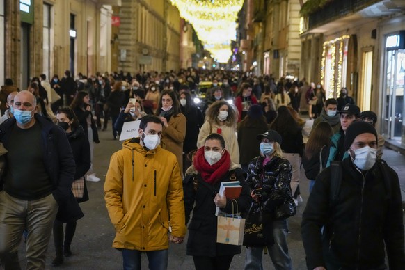 People wearing face masks walk on the street, in Rome, Thursday, Dec. 30, 2021. Italy surged to a record 98,030 new cases of COVID-19 infections Thursday, an increase of 25% in one day. The government was meeting later to consider reducing the quarantine for vaccinated people, amid forecasts that the increasing numbers of infections could place more than 2 million people in quarantine after close contact with infected people. (AP Photo/Andrew Medichini)