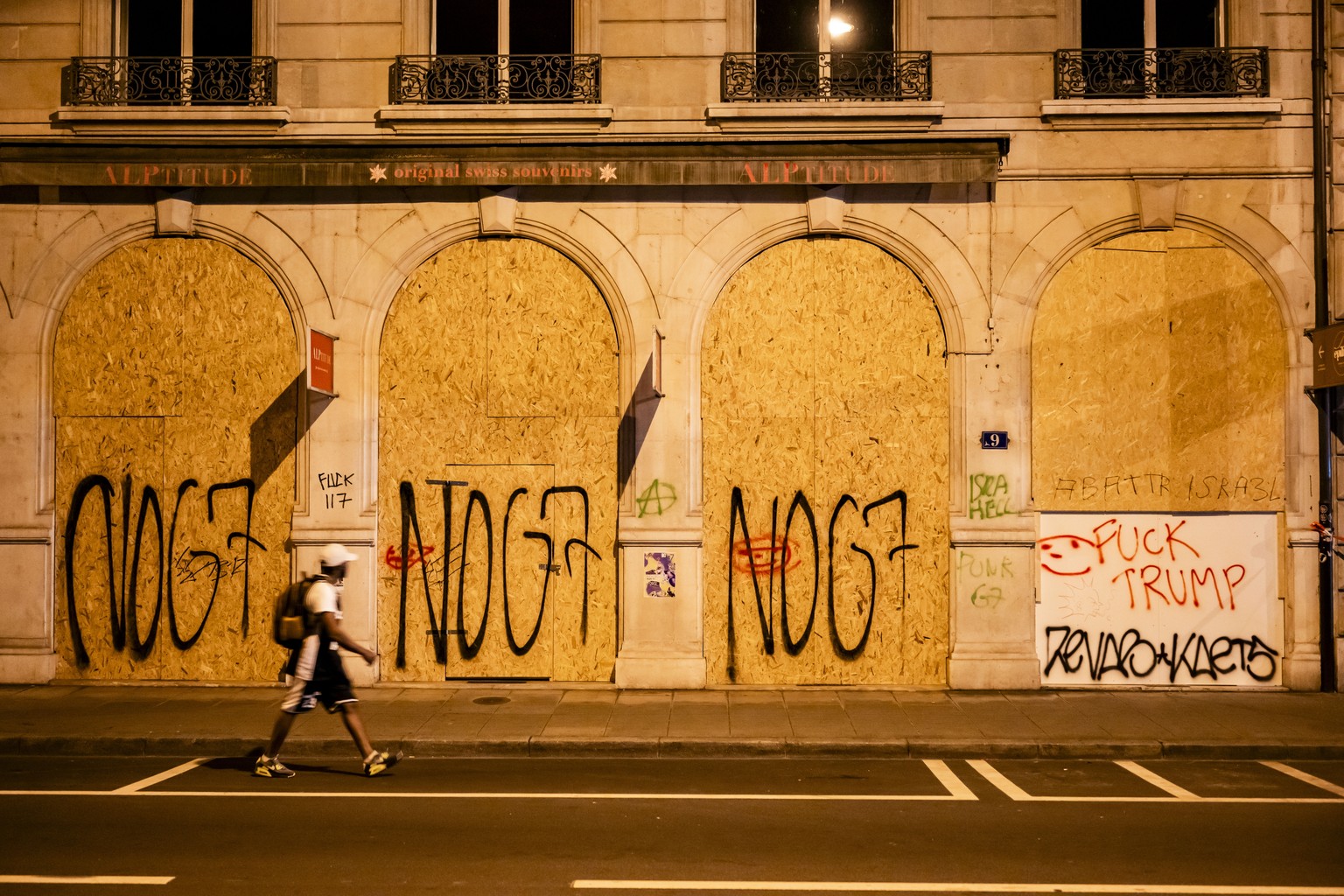 epa13037519 A person walks past wooden panels spray-painted with 'No G7 and Fuck Trump', installed to protect a facade during a demonstration against the G7 summit in Geneva, Switzerland, 15 ...