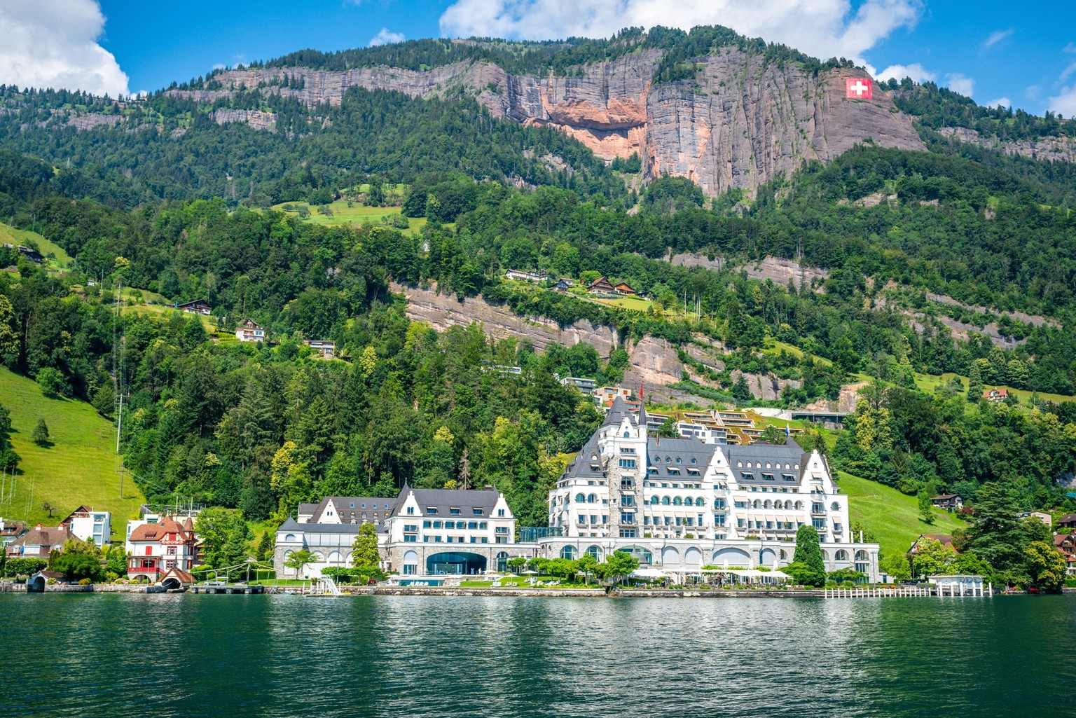 Vitznau Switzerland , 28 June 2020 : Luxury Park Hotel Vitznau taken from Lucerne lake and giant Swiss flag attached to the mountains in Switzerland