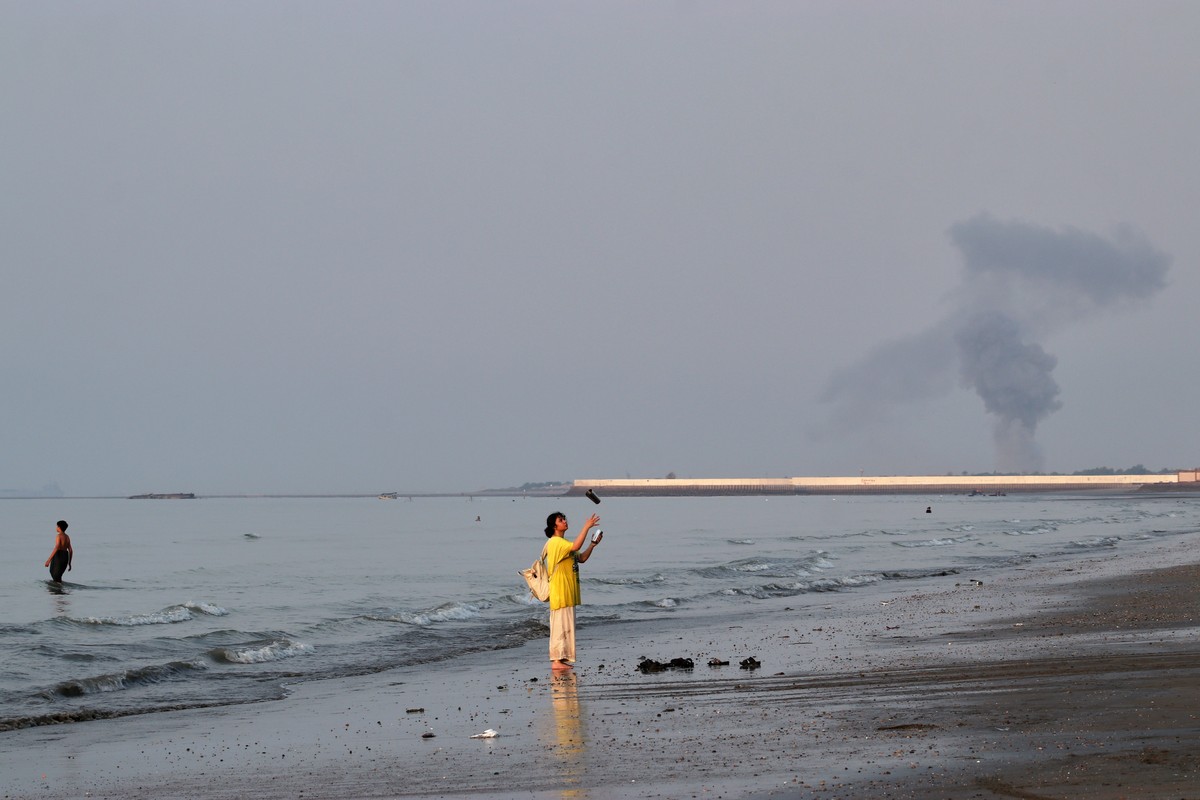 KEYPIX - A woman stands at the water's edge along the Strait of Hormuz as a plume of smoke rises in the background following an explosion, off Bandar Abbas, Iran, Monday, July 13, 2026. (KEYSTONE ...