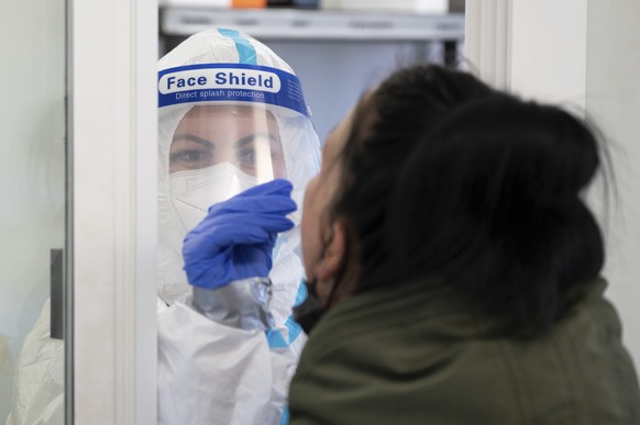 Lavinia Israel, a testing center employee, takes a sample from a customer for a quick test at a Corona testing center at the Kaufpark Nickern shopping center in Dresden, Germany, Friday, Dec. 3, 2021. ...