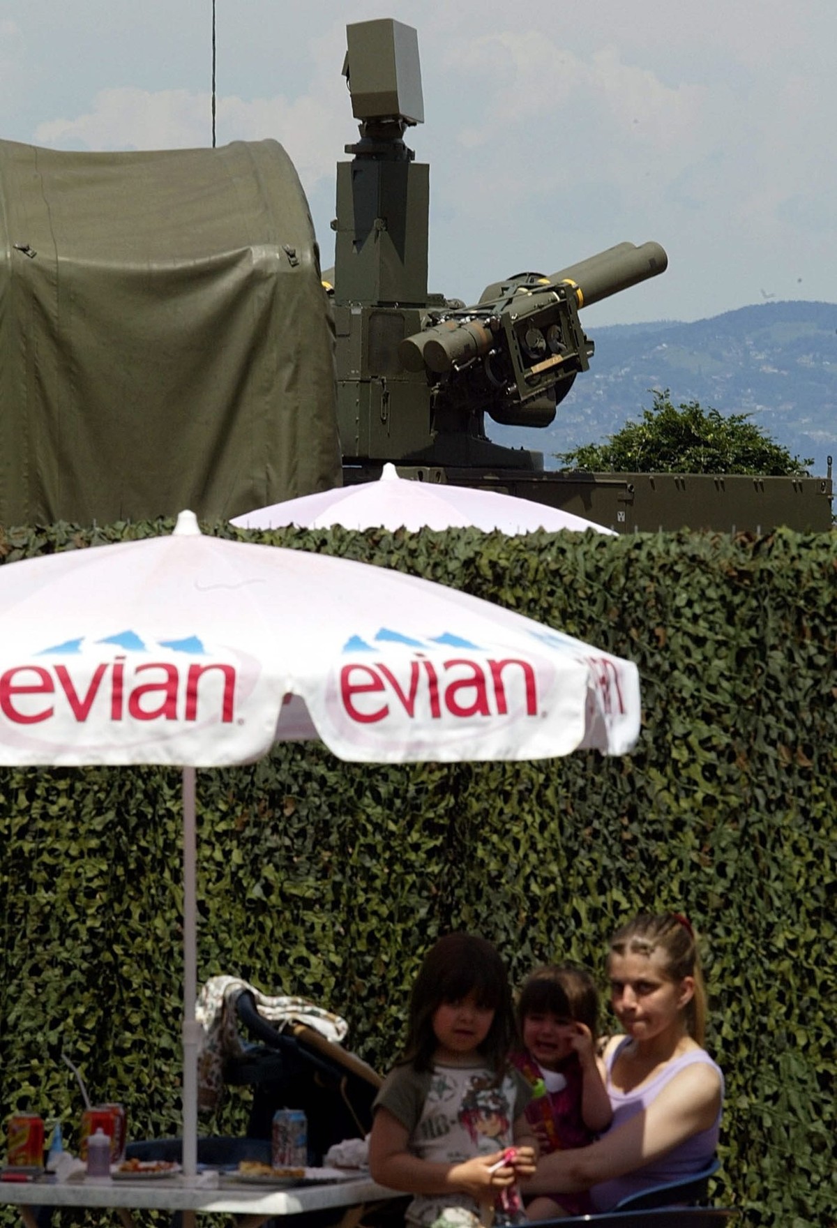 Locals enjoy refreshments next to a temporary military zone with a French military rocket launcher overlooking Lake Geneva from the shores in Evian, Saturday, 31 May 2003. The security has been steppe ...