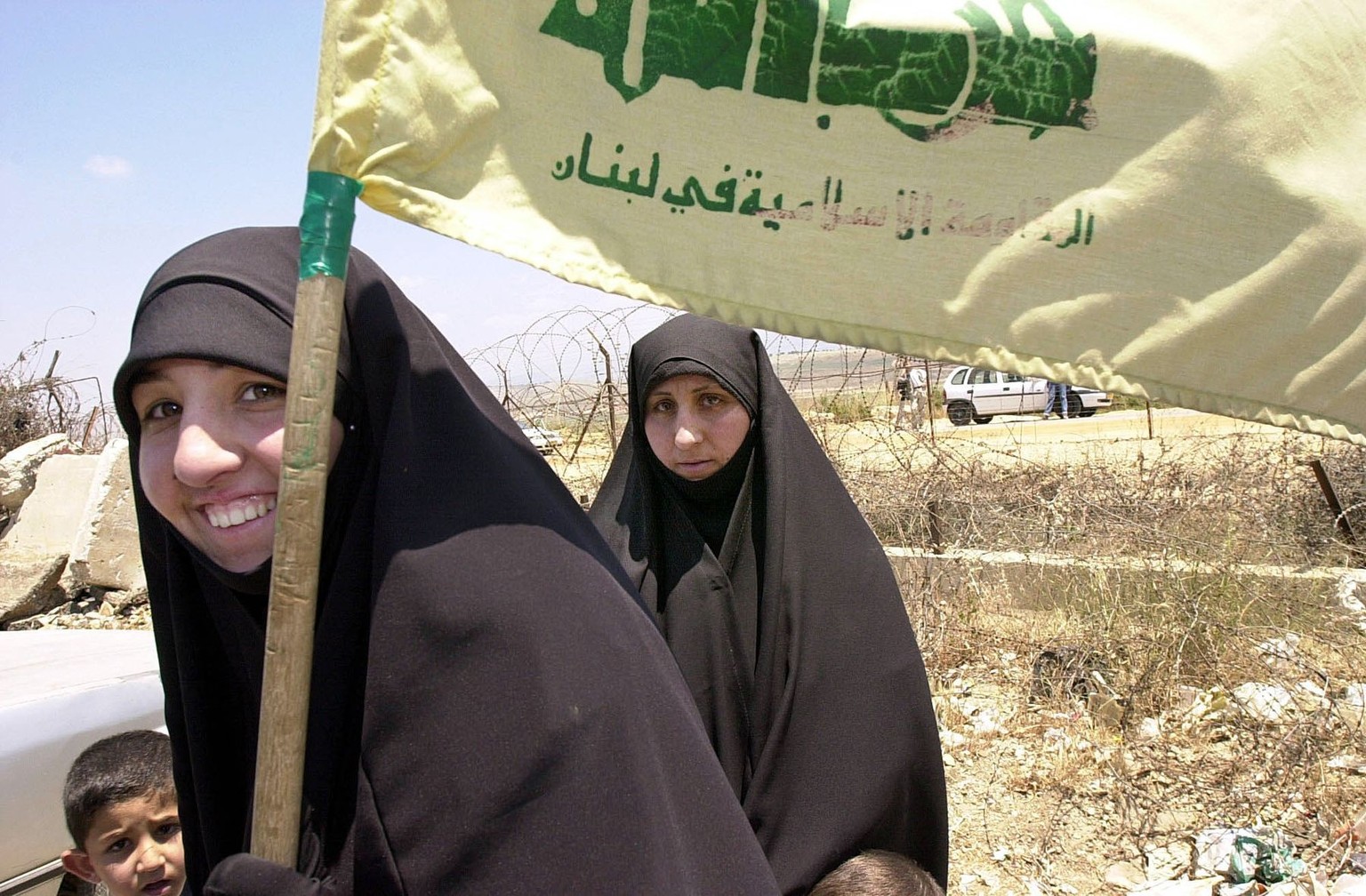 Shiite Lebanese women carry a Hezbollah flag next to the fence that separates Lebanon from Israel in the border town of Kfar Kila, some 120 km. south of Beirut, Wednesday, May 24, 2000. Israel complet ...
