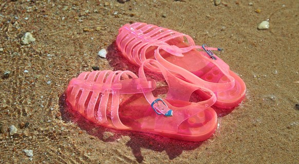 Pink Women&#039;s JELLY SANDALS on a sea shore. LADIES FLAT JELLIES SUMMER BEACH SHOES. Sand background