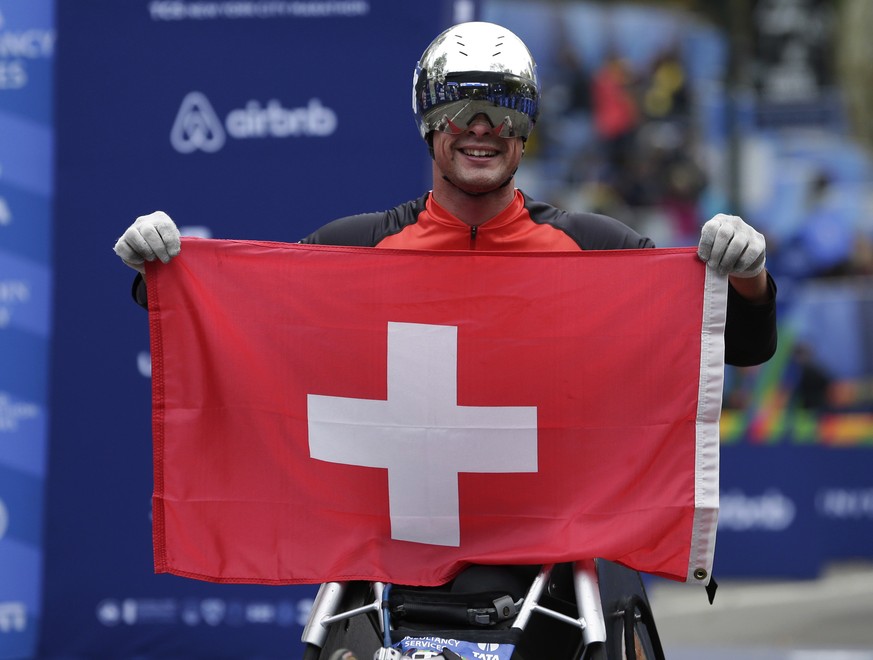 Marcel Hug of Switzerland holds up a flag after crossing the finish line first in the men&#039;s wheelchair division of the New York City Marathon in New York, Sunday, Nov. 5, 2017. (AP Photo/Seth Wen ...