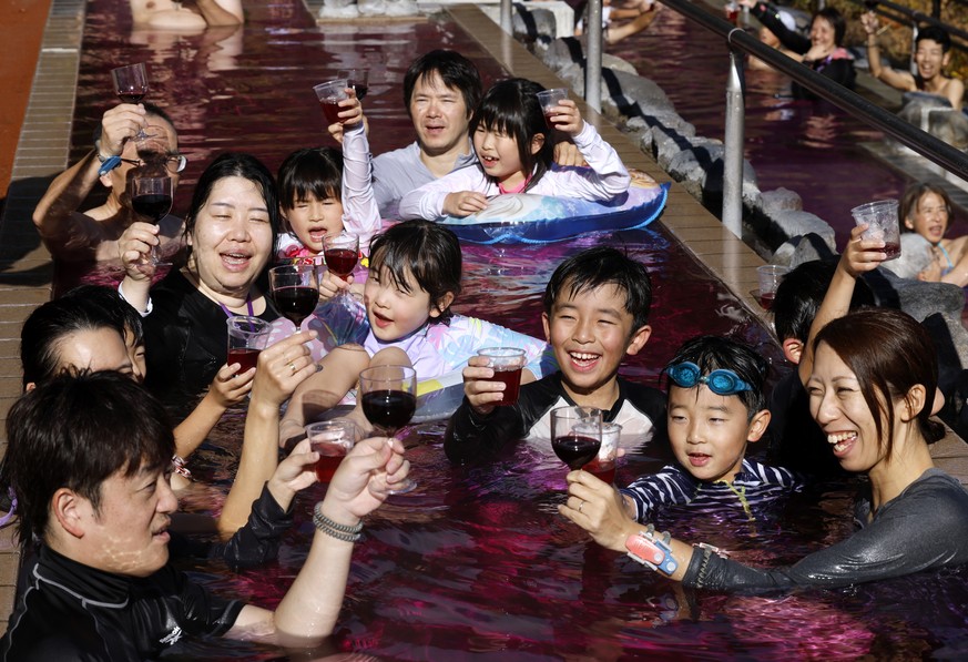 epa12537243 People bathe in a red-colored hot water bath holding glasses filled with 2025 Beaujolais Nouveau wine or grape juice on the day of the Beaujolais Nouveau official release at Hakone Kowakie ...
