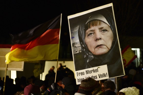 FILE - In this Jan. 12, 2015 file picture a protestor holds a poster with an image of German Chancellor Angela Merkel wearing a headscarf in front of the Reichstag building with a crescent on top duri ...