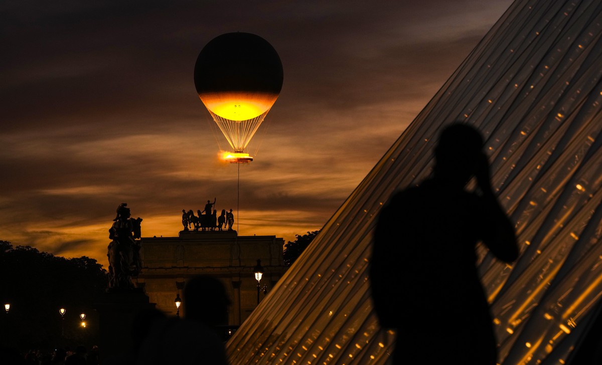 A man takes photos as the Olympic flame rises on a balloon seen from the courtyard of the Louvre during the 2024 Summer Olympics, Sunday, Aug. 4, 2024, in Paris, France. (AP Photo/Francisco Seco)